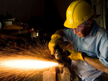 Manufacturing.  A man grinds metal causing sparks to fly everywhere.  