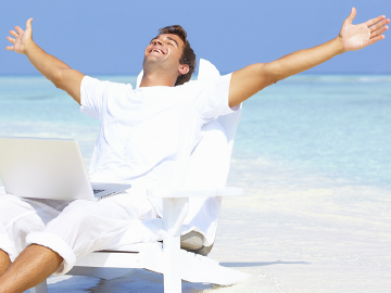 Man on tropical beach working happily on his computer with arms spread high over head