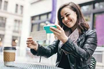 woman takes picture of check with her phone as she's breaking with a coffee