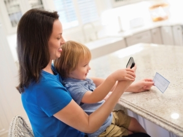 Mom using mobile check deposit with child at island kitchen