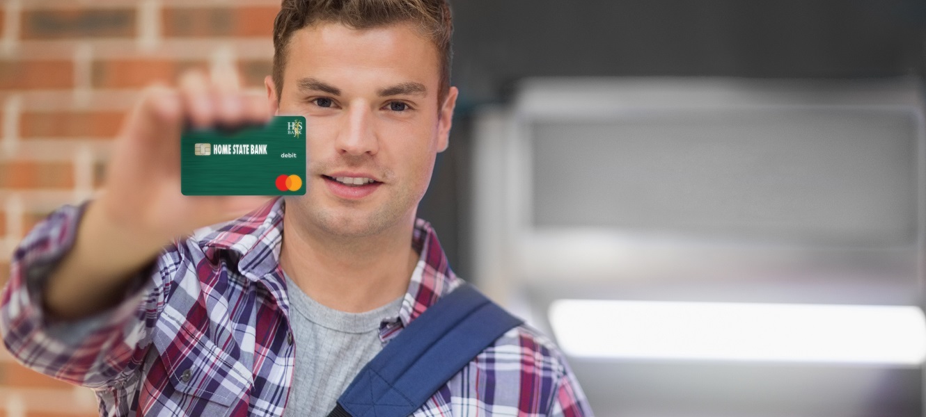 Student Checking and debit card. 
 young male student holding a Home State Bank Debit Card at a bank ATM machine.